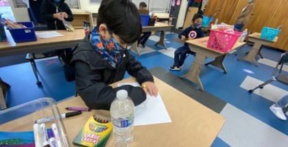 A closeup of a young student wearing a mask and working at a desk