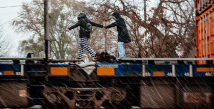 Two children on their way to school help each other over a parked train.